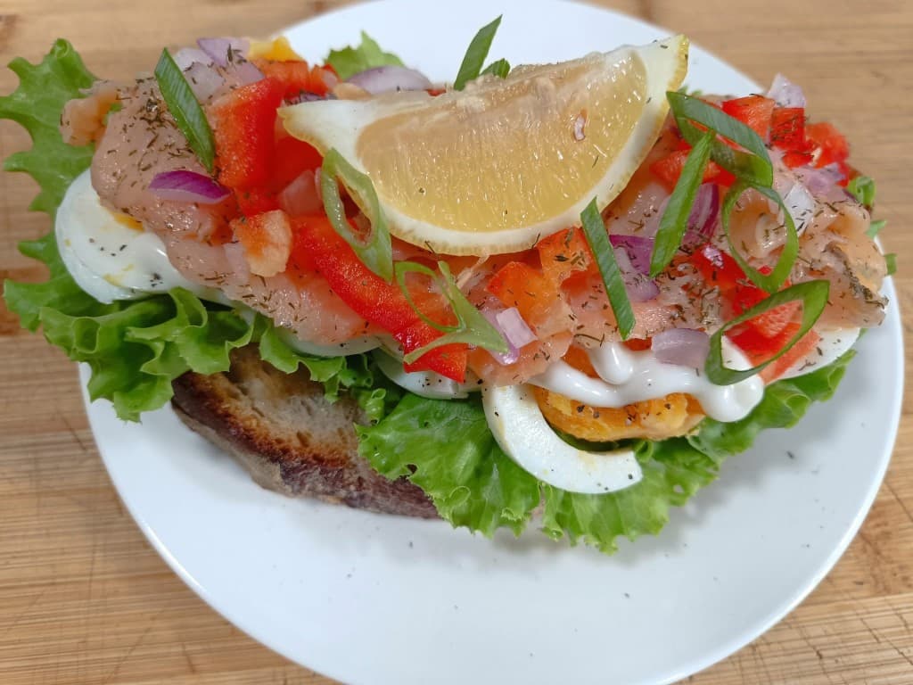 Open-faced smoked salmon smørrebrød with egg, vegetables, and lemon